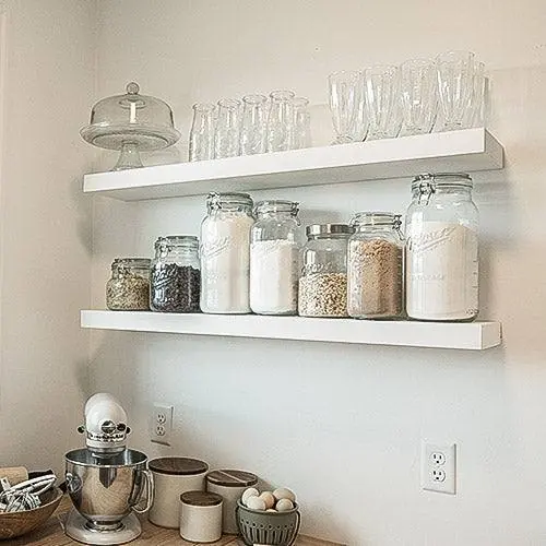 A floating shelf mounted in a white kitchen, styled with kitchen items, shown in a real installed setting. Photo from ultrashelf.com.