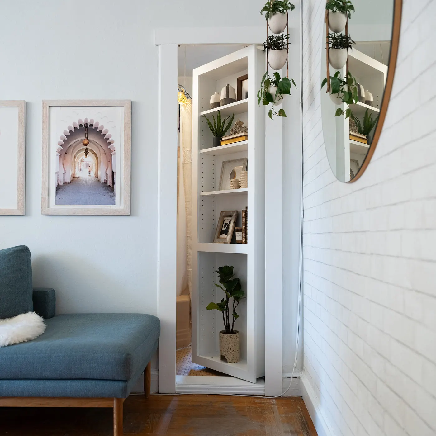 A Murphy Door® hidden door open, revealing a hallway with framed art beyond a blue sofa. Photo from murphydoor.com.