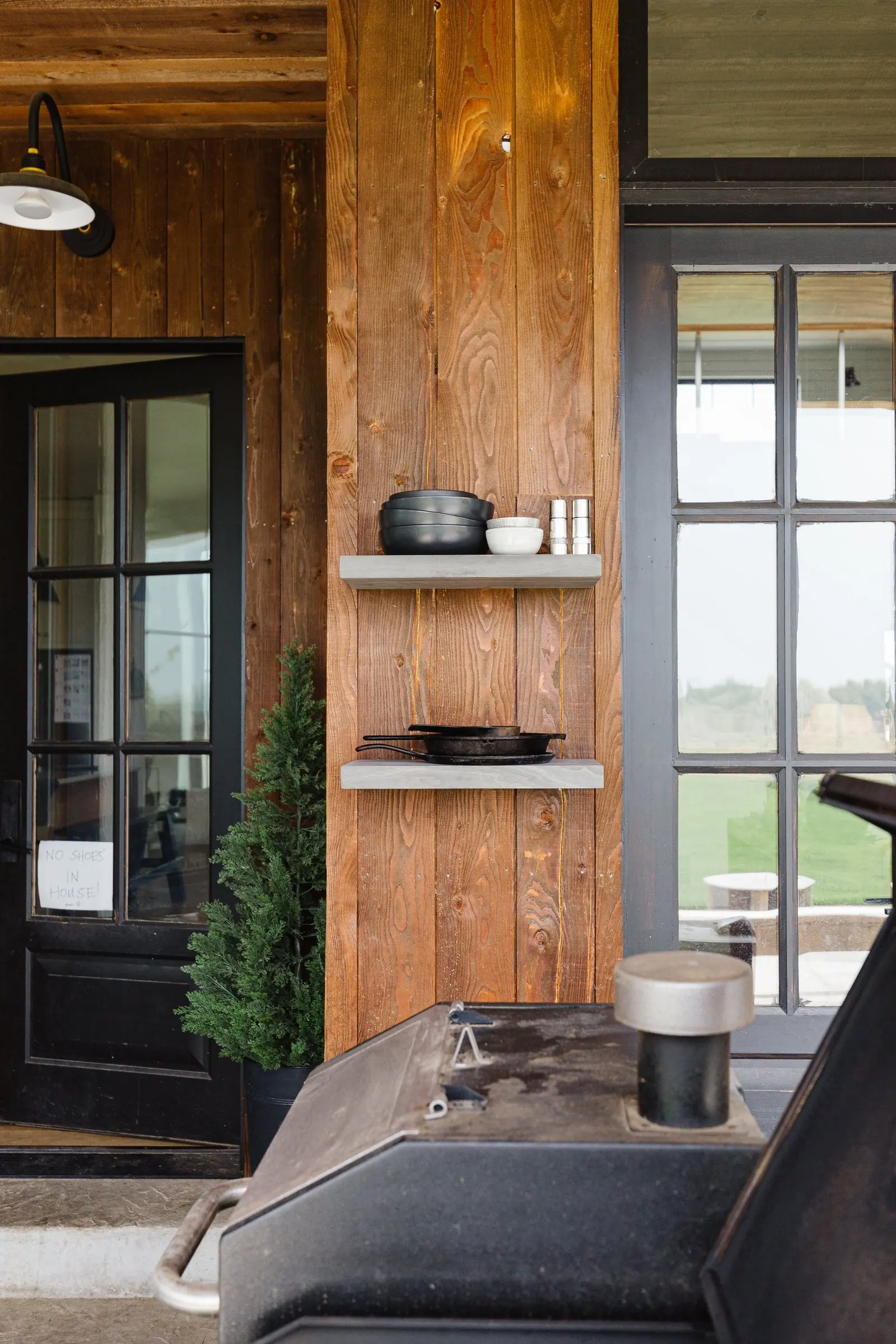A great room with textured wood paneling, floating shelves, and black steel doors opening to the landscape view. Photo from ultrashelf.com.