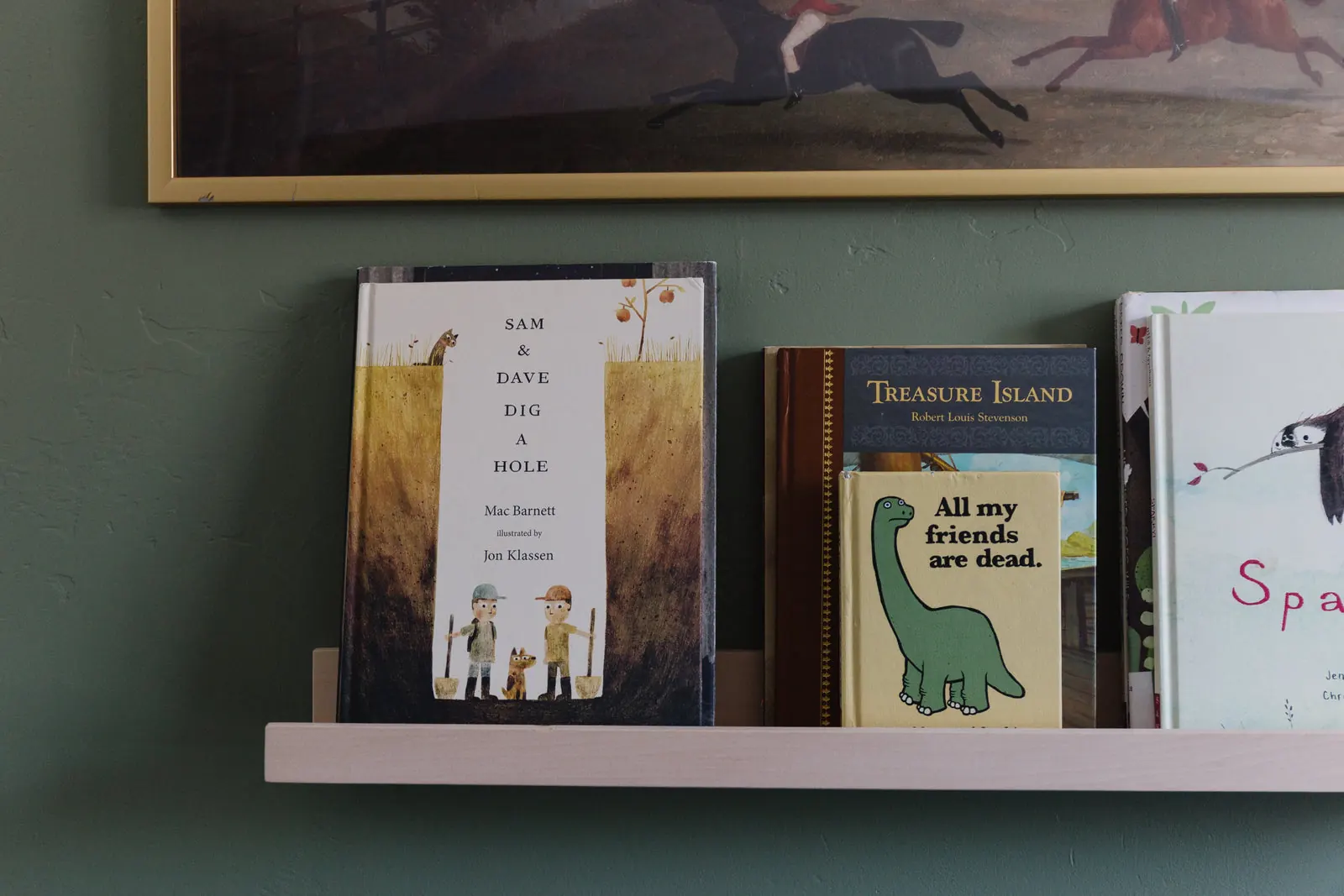 A long picture ledge lined with books on a deep green wall. Photo from ultrashelf.com.