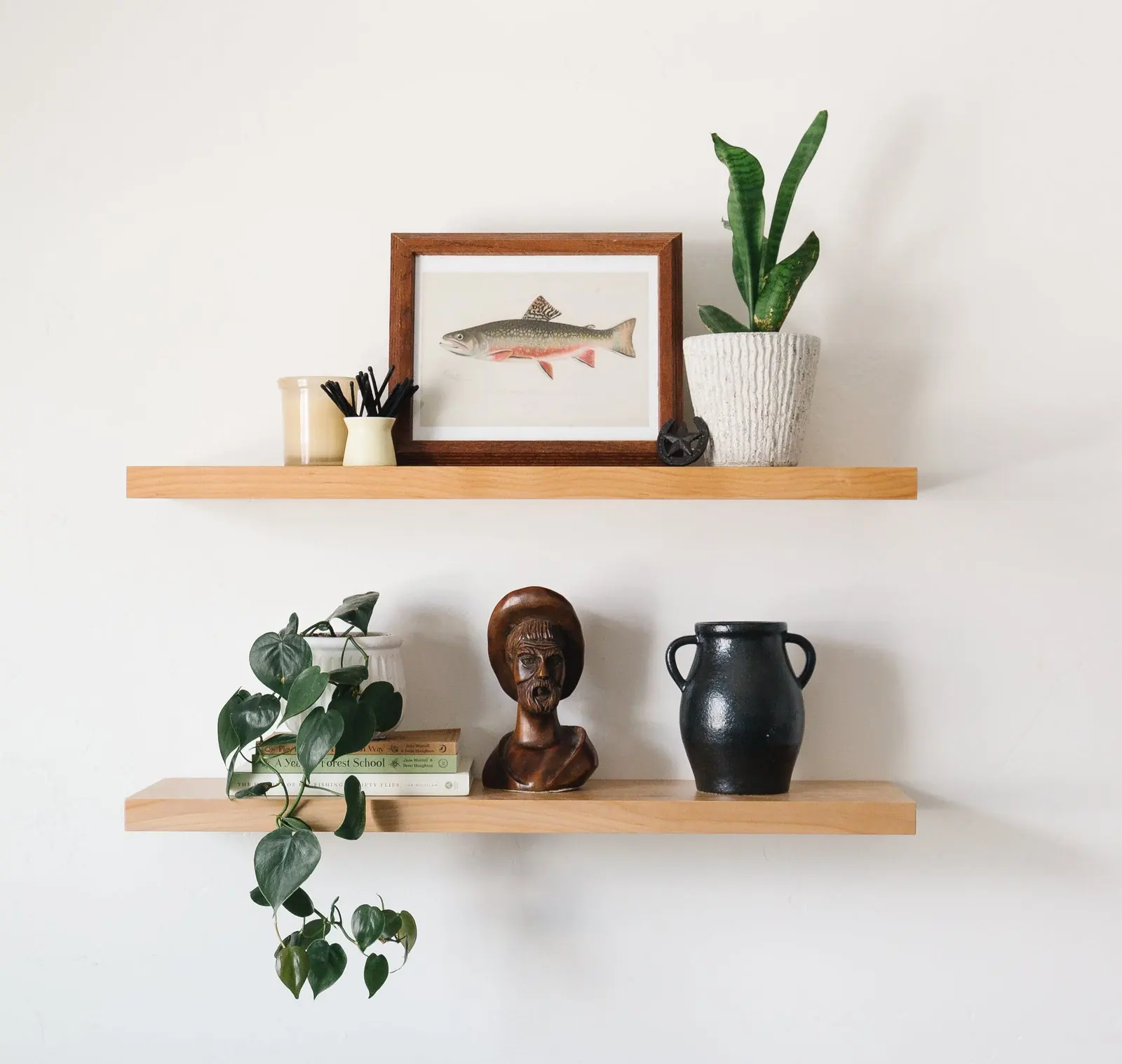 Two stacked floating shelves styled with art, plants, and ceramics on a neutral wall. Photo from ultrashelf.com.